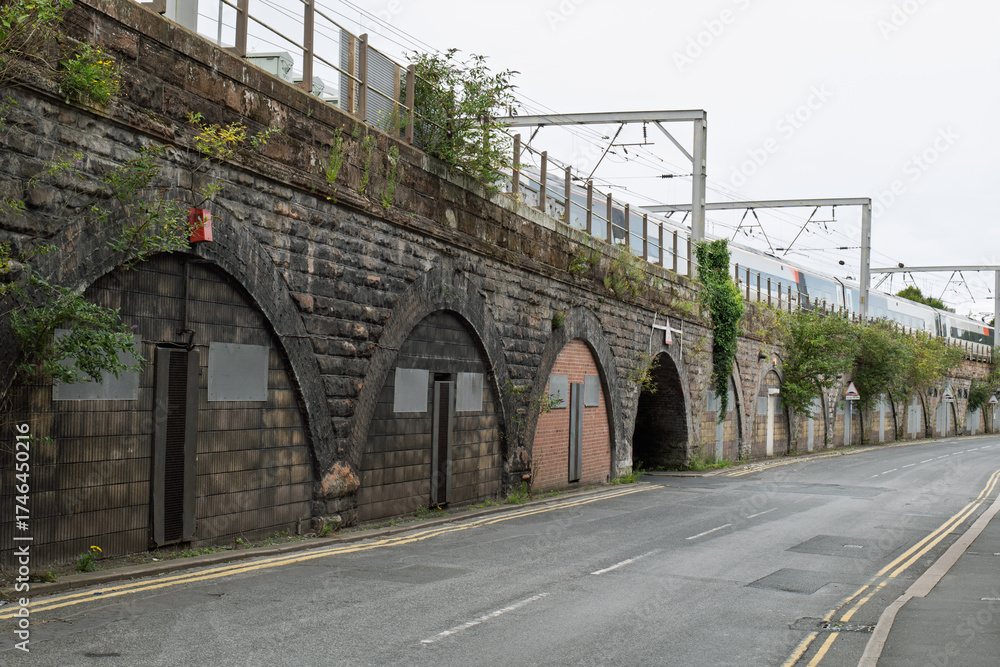 Fototapeta premium Railway viaduct storage arches sealed with doors and metal panels beneath active train tracks, highlighting urban decay, history, and industrial architecture.