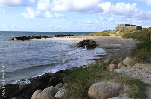 Landscape photo with a view of a bay of sea, a sandy beach with large stones in the foreground and a bunker on the coast at Cape Grenen, in Skagen, northern Denmark