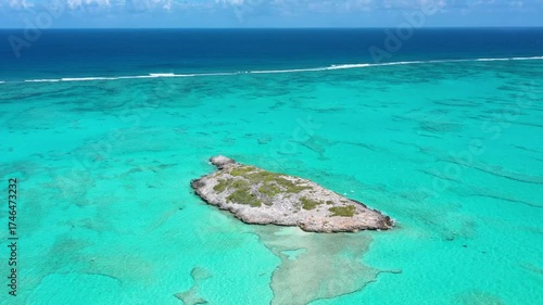 Aerial view of a small, isolated island in a vast tuquoise ocean.