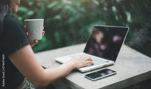 Картината върху платно Woman working on laptop with coffee cup in hand at outdoor table in garden