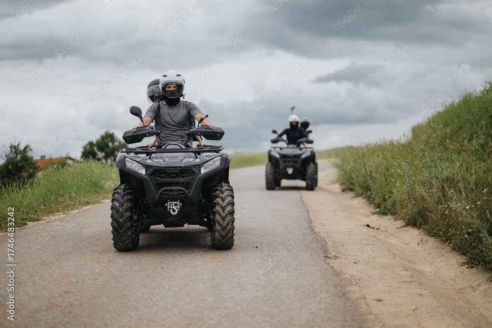 Fototapeta premium Two friends riding ATVs through a peaceful countryside road, enjoying outdoor adventure surrounded by nature.