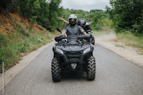 Two individuals wearing helmets ride all-terrain vehicles on a paved road through a scenic forest environment, enjoying an adventurous outdoor activity together.