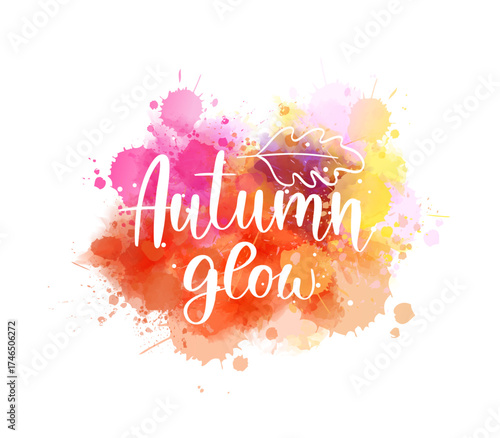 Colorful handwritten text 'Autumn glow' on watercolor orange paint splashes. Seasonal modern calligraphy lettering text