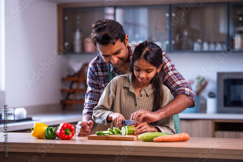 Indian father and daughter chopping cucumber, sharing joyful bonding at home