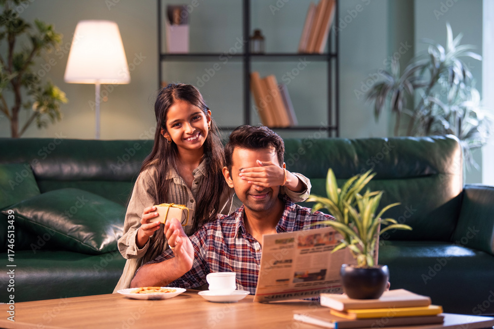 Fototapeta premium Indian Daughter surprising father with gift, hugging and sharing loving family moment at home