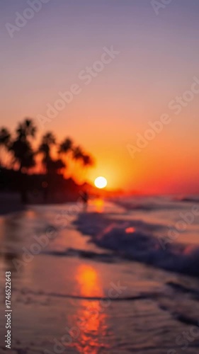 This mesmerizing, out-of-focus video captures a serene tropical beach at sunset, bathed in an ethereal glow. Gentle waves softly undulate towards the shore, reflecting the magnificent, fiery orb of th