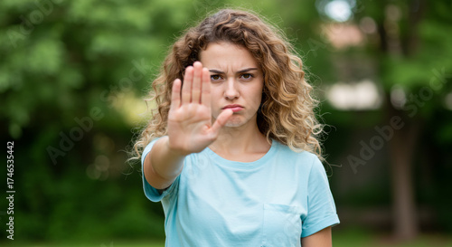 Young woman with curly hair making a stop gesture with her hand, conveying a clear message of refusal or boundary setting outdoors