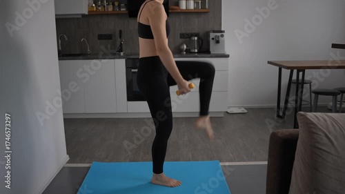 Unrecognizable woman in dark sportswear exercising at home. Kitchen background. Home workout.
