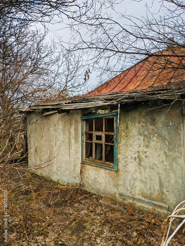 The exterior of an old abandoned house in a village in Ukraine. The walls of the house are made of clay (Mazanka) and the iron roof is rusty