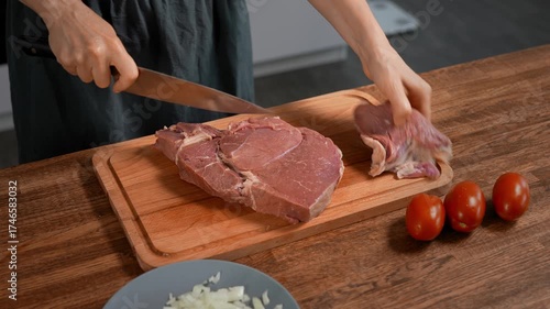 Woman cutting large beef piece on wooden board. Preparing steaks.