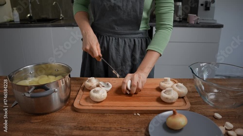 Woman cutting mushrooms on wooden board. Close-up, kitchen prep.