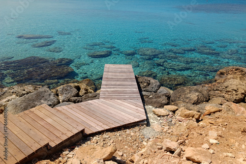 A wooden pier with a walkway leading to the azure sea. A serene tropical seascape with clear turquoise water. Summer vacation, holidays, ocean relaxation