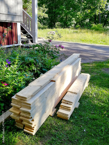 New wooden boards are stacked near the house. Walls are being replaced in an old building