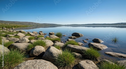 Serene lake view with rocky shore, grass, reflecting calm waters, blue sky