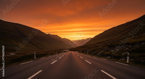 Straight road vanishing between dark hills, sunset sky burning orange above