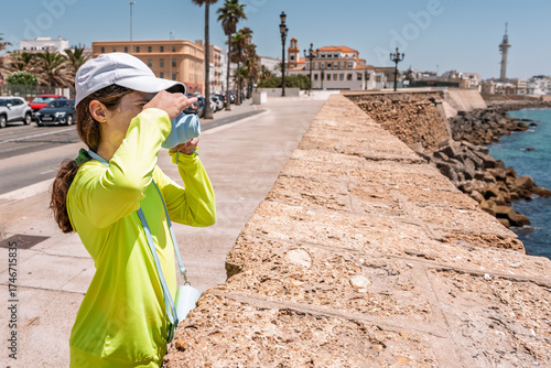 A young girl on summer vacation, taking a picture of the ocean with her polaroid camera on the coast of Cadiz, Spain in Europe. 