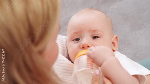 Woman holds and feeds baby with care and love. Baby sucks on formula from bottle, closing his eyes and falling asleep. Alternative to breastfeeding, nanny and infant care, maternal care
