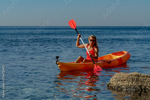 Woman, kayak, paddling a bright orange boat in the clear blue sea, enjoying summer vacation