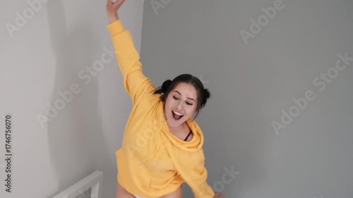 Pretty girl in a yellow sweater having fun on the bed - jumping and dancing. brunette