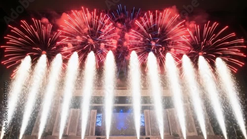 night display features fireworks bursting in the dark sky A grand stage below is lit by symmetrical row of golden vertical pyrotechnics highlighting architectural elements and central star