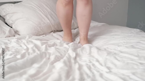 Pretty girl in a yellow sweater having fun on the bed - jumping and dancing. brunette