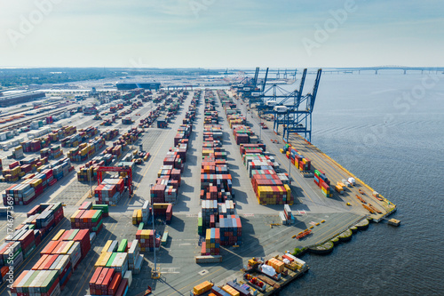 Aerial view of a vast port painted with a vibrant tapestry of stacked shipping containers under a vast sky, cranes reaching out to the water, Baltimore, Maryland, United States.