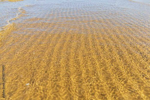 Fototapeta Naklejka Na Ścianę i Meble -  Intricate sand ripples visible beneath clear, shallow water with gentle waves, at the serene coast of the Baltic Sea, creating natural abstract patterns