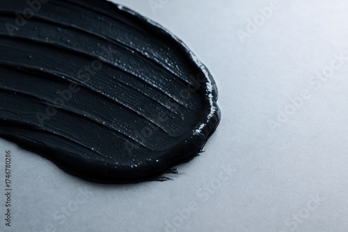 Close-up of dark graphite slurry with smooth glossy texture spread on a gray surface
