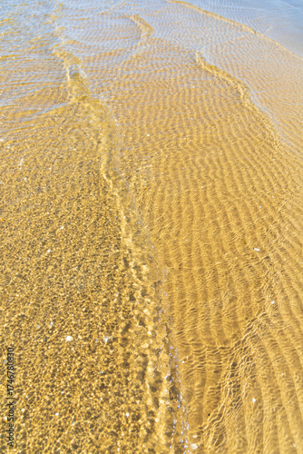 Fototapeta Naklejka Na Ścianę i Meble -  Intricate sand ripples visible beneath clear, shallow water with gentle waves, at the serene coast of the Baltic Sea, creating natural abstract patterns