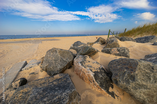 Fototapeta Naklejka Na Ścianę i Meble -  Large rocks and sandy dunes at beach entrance by the Baltic Sea under blue sky with scattered clouds