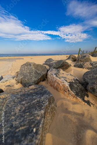 Fototapeta Naklejka Na Ścianę i Meble -  Large rocks and sandy dunes at beach entrance by the Baltic Sea under blue sky with scattered clouds