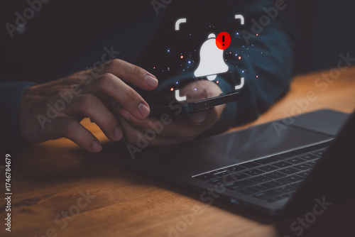 Notification alert concept showing a person checking smartphone beside laptop with glowing bell icon, symbolizing mobile communication, message alert, and digital notification system.