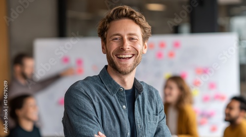 Cheerful man smiling in a modern office environment, engaging with colleagues in a collaborative workspace.