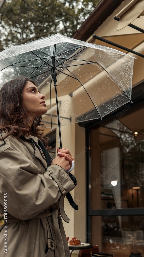 Fototapeta premium Girl in trench coat under a clear umbrella on a rainy day