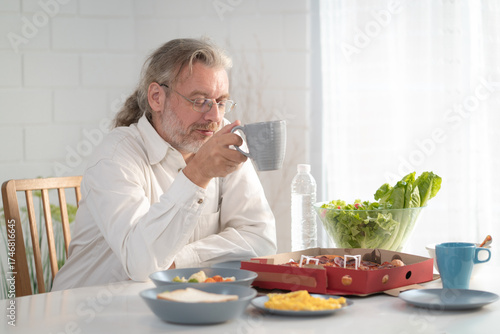 Senior elderly older grandfather stay at home with painful face sitting alone on eating table in house. Depressed elderly retired man upset feeling unhappy. Lonely and missing his family at home	