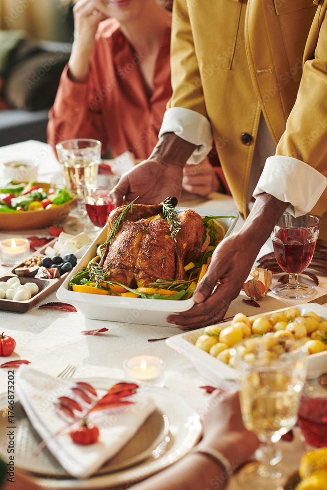 Fototapeta premium Black man serving roasted turkey at Thanksgiving dinner table surrounded by diverse group of adults, enjoying holiday meal together with various dishes and drinks visible on table