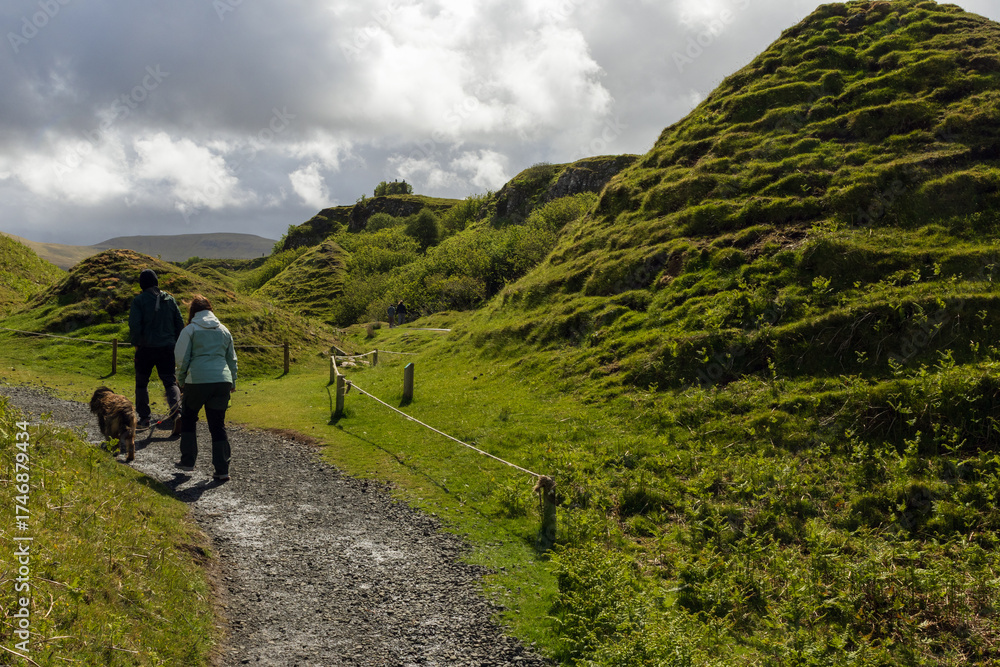 Fototapeta premium Back view of visitors at the Fairy Glen with green hills, Isle of Skye, Scotland