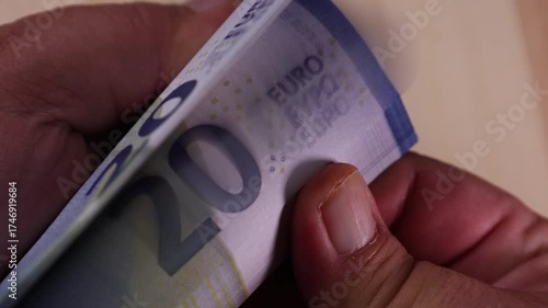 Close-up overview of a bank stack of 20 euro bills and flipping through the stack of bills in hands.
