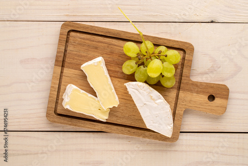 Fragrant camembert cheese with grapes on a wooden table, top view.