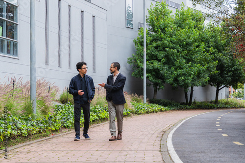 Two young professional men walking and conversing outdoors on a college campus