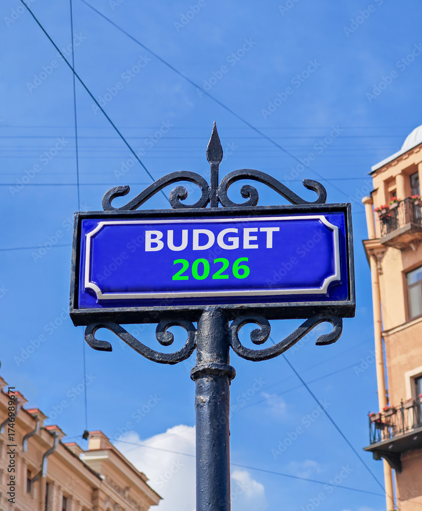 Obraz premium Budget 2026 symbol. Concept words Budget 2026 on beautiful blue road sign. Beautiful blue sky and buildings background. Business and budget 2026 concept. Copy space.