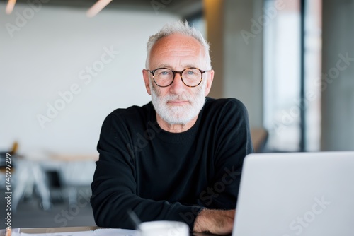 Elderly man with glasses working on laptop at table in modern setting