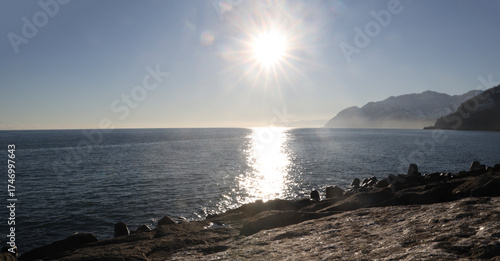 Fototapeta Naklejka Na Ścianę i Meble -  Dark rock massif on the sea coast. Sun setting behind rocky cliffs. Sea coast, waves, orange-blue sky. Sarpi, Sarp. Border between Turque and Georgia. Black Sea.