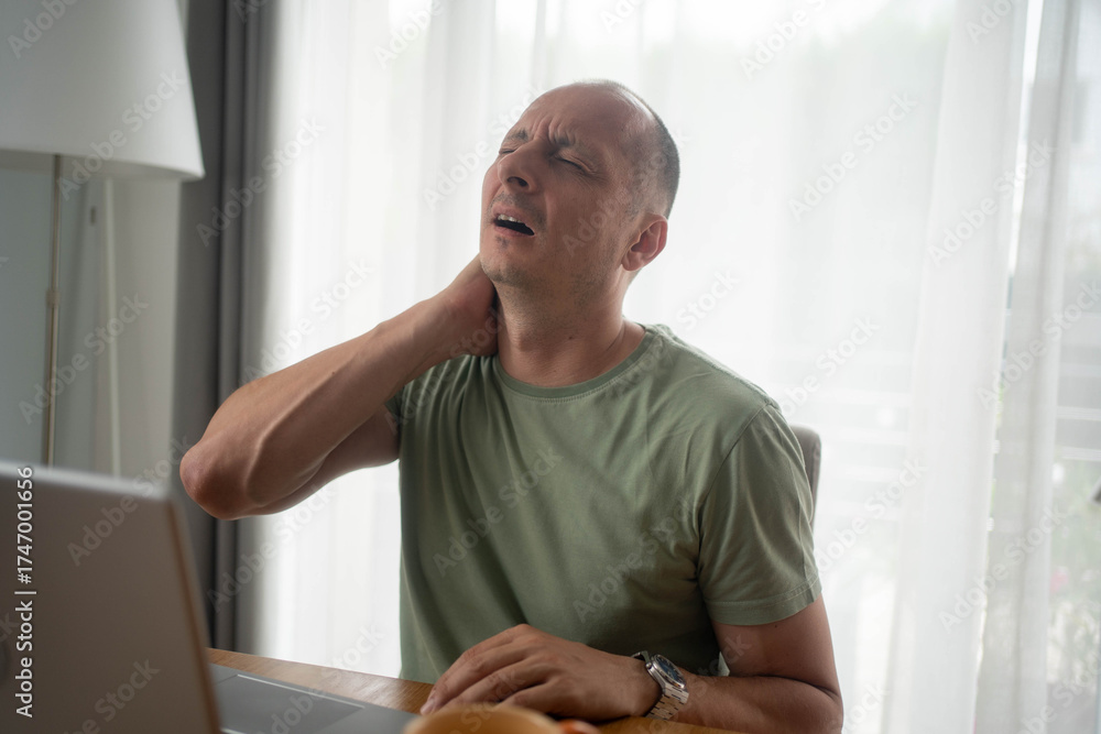 Fototapeta premium Tired man working from home on laptop suffering from neck pain