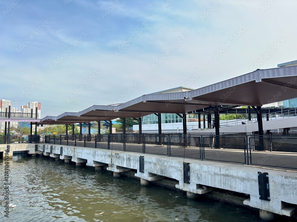 Fototapeta premium Exterior shot of a modern waterfront terminal structure with tiered brown roofing and concrete pillars. Ideal for urban transport, city infrastructure, water travel, or architectural backgrounds