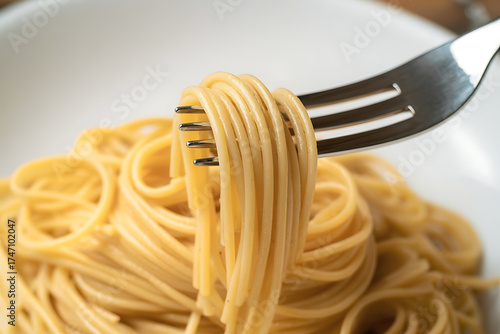 Close-up of spaghetti twirling around a silver fork over a white plate.