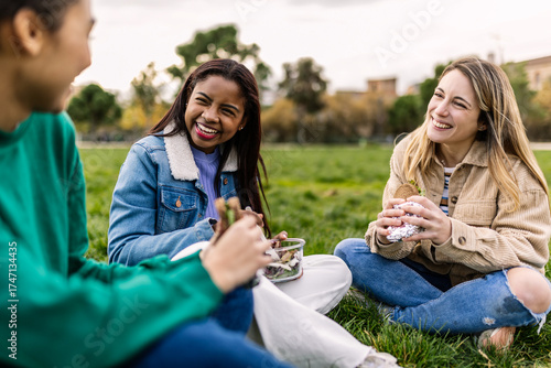 Obraz na plátně Group of happy young women students laughing while having lunch outdoors on green grass