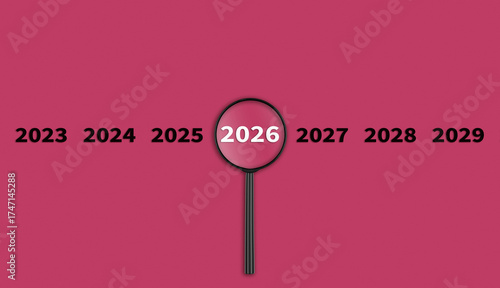 Lens, magnifying glass focusing on the year 2026 on a red background. Financial or stock market strategies and past and future events.