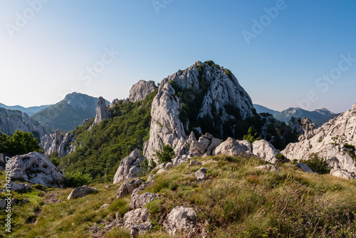 The stunning white limestone peaks of the Velebit mountain range stand tall against a clear blue sky, with a rugged, grassy landscape in the foreground, showcasing Croatia's raw natural beauty.