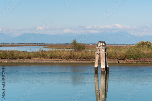 Paesaggio della lagina di Venezia con le barene, una briccola, tipico palo per la navigazione, e le montagne sullo sfondo